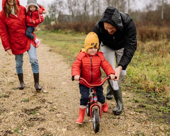 Happy family walking outdoors in fall, teaching child to ride bike.